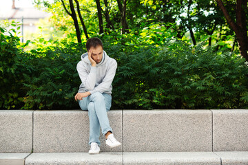 Stressed man robbed during vacation: worried and tired male sit on pavement in park without backpack and baggage. Guy lost money and smartphone. Tourist with stolen wallet pensive looking for solution