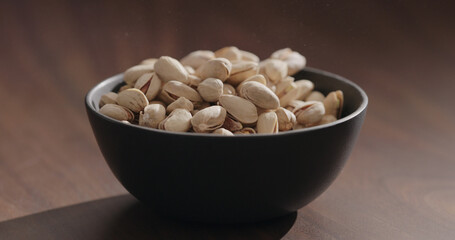 Roasted salted pistachios in black bowl on walnut table