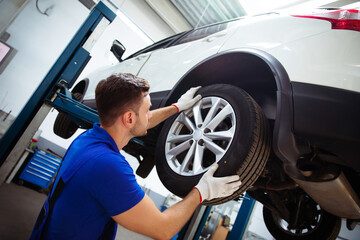 Handsome professional car mechanic changes a wheel on a car or carries out a tire change at a...