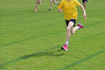 Group of unrecognizable runners running fast on grass running track outdoors.