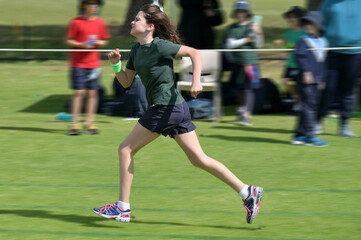 Naklejka premium Motion blur of a young girl (female age 11-12) running fast on grass running track outdoors.