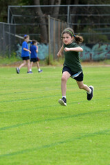 Determent young girl (female age 07-08) running relay race on grass running track outdoors.