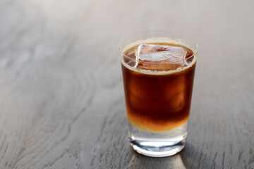 Espresso tonic with clear ice cube in tumbler glass on oak wood table with copy space
