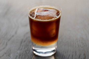 Espresso tonic with clear ice cube in tumbler glass on oak wood table with copy space