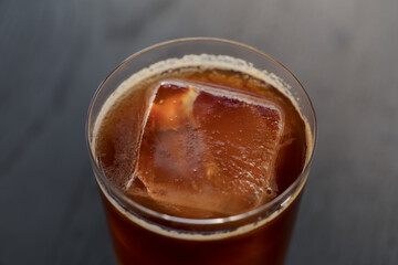 Closeup espresso tonic with clear ice cube in tumbler glass on oak wood table