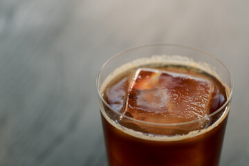Espresso tonic with clear ice cube in tumbler glass on oak woo table with copy space