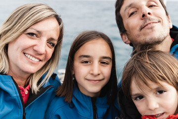 Fototapeta premium Happy family doing selfie with mobile phone at luxury boat with ocean on background - Hapinness, joy and love concept - Focus on mother face