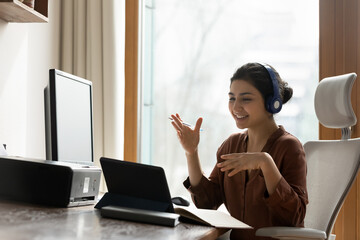 Social distance in office work. Young indian female team leader in earphones meet staff online...