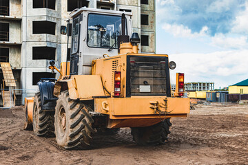 Heavy wheel loader with a bucket at a construction site. Equipment for earthworks, transportation and loading of bulk materials - earth, sand, crushed stone.