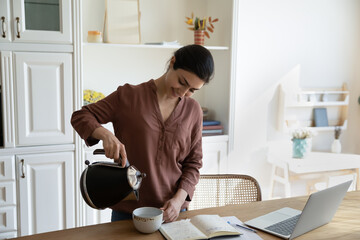 Quick tea break. Smiling indian female freelance worker take pause in online work at home office to make cup of coffee. Young biracial woman brew tea in mug pour hot water from modern electric kettle - Powered by Adobe