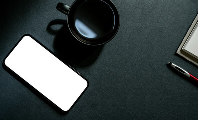 Top view blank screen smartphone, cup of coffee, pen and notebook on black leather background.