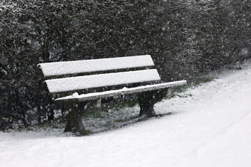 A wooden bench covered with snow during a blizzard