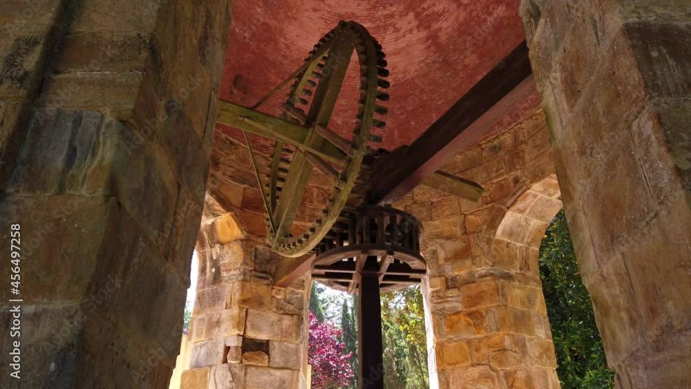 Canvas Prints A low angle shot of a vintage water industrial machine with gears hanged up between old stony walls