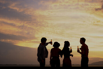 Fototapeta na wymiar Silhouette Groups of friends or couples dance and drink at the campsite near the lake at sunset. Twilight time.