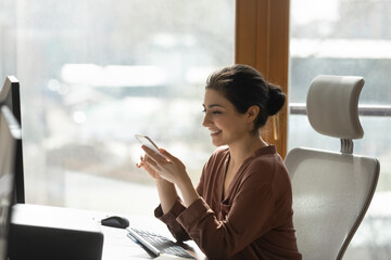 Modern tech in office. Happy young mixed race woman manager sit at desk by computer messaging on...