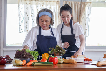 happy asian young daughter and senior mother cooking online  class on tablet together making fresh vegetables food in kitchen at home
