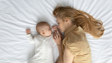 Tired mom and cute peaceful baby sleeping on mattress with white sheet. Calm young mother and...