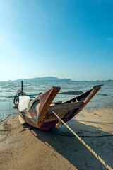 Fototapeta na wymiar Traditional long tail boat with oars moored on the sand of a Phuket beach, Thailand