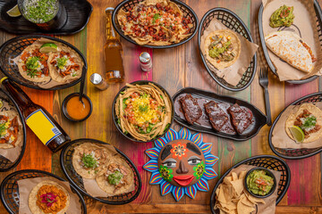 Fototapeta na wymiar Top view image of set of Mexican food dishes mango salads, quesadillas, cochinita pibil guacamole, tacos al pastor, nachos with chili and cheese, brownie and wooden table