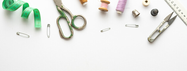 Flat lay composition with threads, scissors, buttons, needles, pins and other sewing accessories on white background. Long banner, top view, copy space, flat lay, mock up. Spase for text