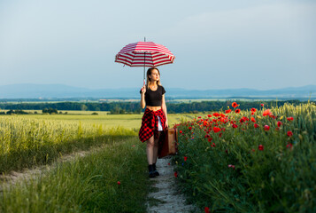 Young woman with umbrella and suitcase walking down on countryside road