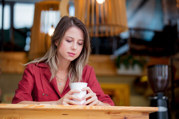 young woman in a red dress with a phone and cup of coffee sits at a table in a cafe