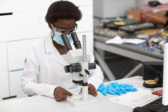 Scientist African American Woman In Face Mask And Gloves Working In Laboratory With Electronic Tech Instruments And Microscope. Research And Development Of Electronic Devices By Color Black Woman.