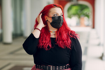 European plus size woman portrait in face mask outdoor street city. Young red pink haired body positive girl.