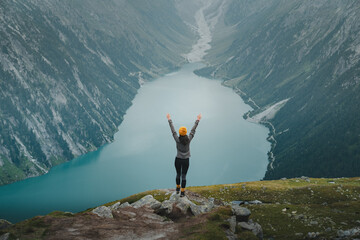 Female hiker celebrating succes on the top of a mountain with with open arms and a splendid view above mountain lake
