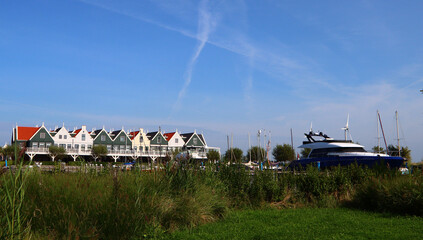 Dutch countryside landscape photo. Cute houses of different colors in a row, empty country rode, green grass, blue sky. Architecture of the Netherlands.