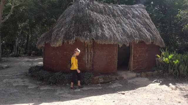 Woman tourist walks into the Chichen Itza traditional pre Columbian Mayan hut home site at historical park.