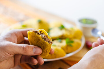 Close up of a hand of person holding a delicious colombian empanada where you can see the meat filling in it