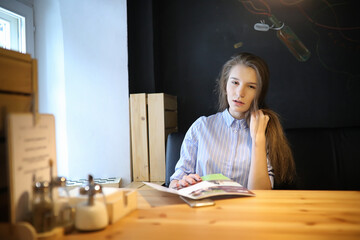 Girl with coffee. Young beautiful girl is sitting in a cafe and drinking coffee in a paper cup. The girl is having breakfast in the coffee house.