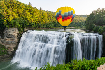 A hot air balloon flying low over the middle falls at Letchworth State Park in New York. The falls...