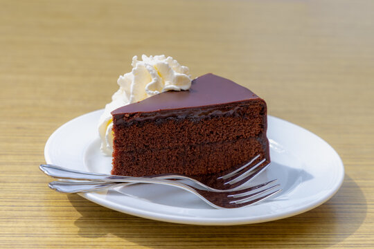 The Original Sacher-Torte on table served with white whipping cream, The cake consists of a dense chocolate cake with a thin layer coated in dark chocolate icing on the top, Famous cake in Austria.