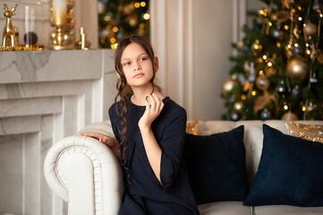 Young girl with dark hair in a Christmas interior in white and gold colors.