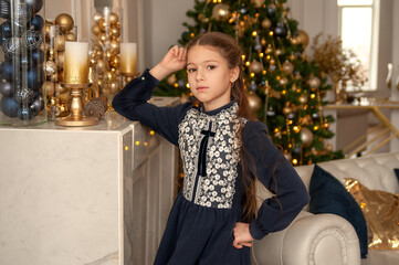 Portrait of a young girl with long hair in a blue dress in a Christmas interior in white and gold colors.