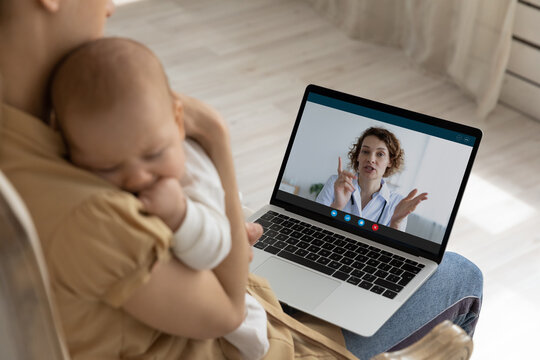 New mom holding cute nappy baby in arms, making video call to doctor, consulting pediatrician from home. Practitioner giving child care consultation, recommendation, advice to young mother