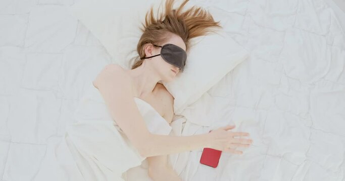 Young woman wakes up from an alarm clock, picks up her phone and is surprised. Overslept.