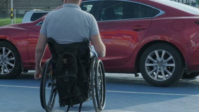 Young handicapped driver getting in red car from wheelchair