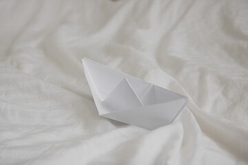 paper origami boat in bed with waves made with bed sheets, natural white crumpled blanket - obrazy, fototapety, plakaty