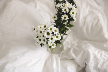 bouquet of white flowers in bed bedroom with  natural bed sheets blanket 
crumpled