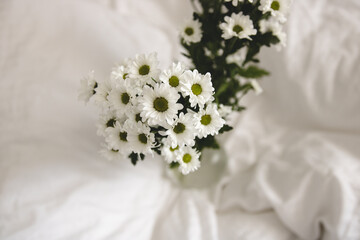 bouquet of white flowers in bed bedroom with  natural bed sheets blanket 
crumpled