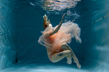 A girl with long dark hair swims underwater in a pink dress and with a crown on her head, like an underwater queen. Fairy tale suitable for advertising