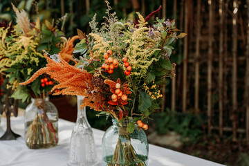 Rustic style. Boho style bouquets on the table in glass vases and jars. Wooden table and white tablecloth