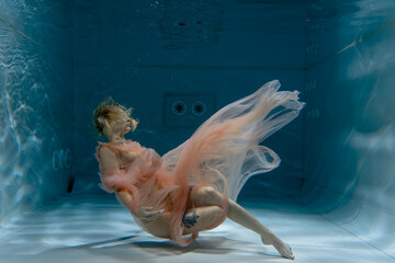 A girl with long dark hair swims underwater in a pink dress and with a crown on her head, like an underwater queen. Fairy tale suitable for advertising