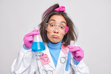 Suprised female scientist conducts experiment with chemicals holds test tube beaker mixes agents analyzes colored liquid in clinical laboratory poses indoor. High school student has chemistry class - Powered by Adobe