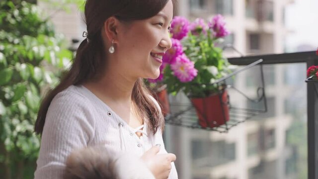 4k slow motion happy young asian woman holding cat pet enjoy looking at her beautiful balcony garden during stay at home