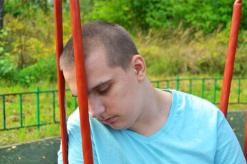 A young autistic guy is sad sitting on a swing alone