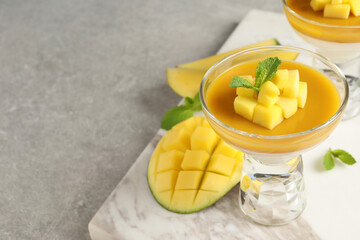 Delicious panna cotta with mango coulis and fresh fruit pieces on light grey table. Space for text